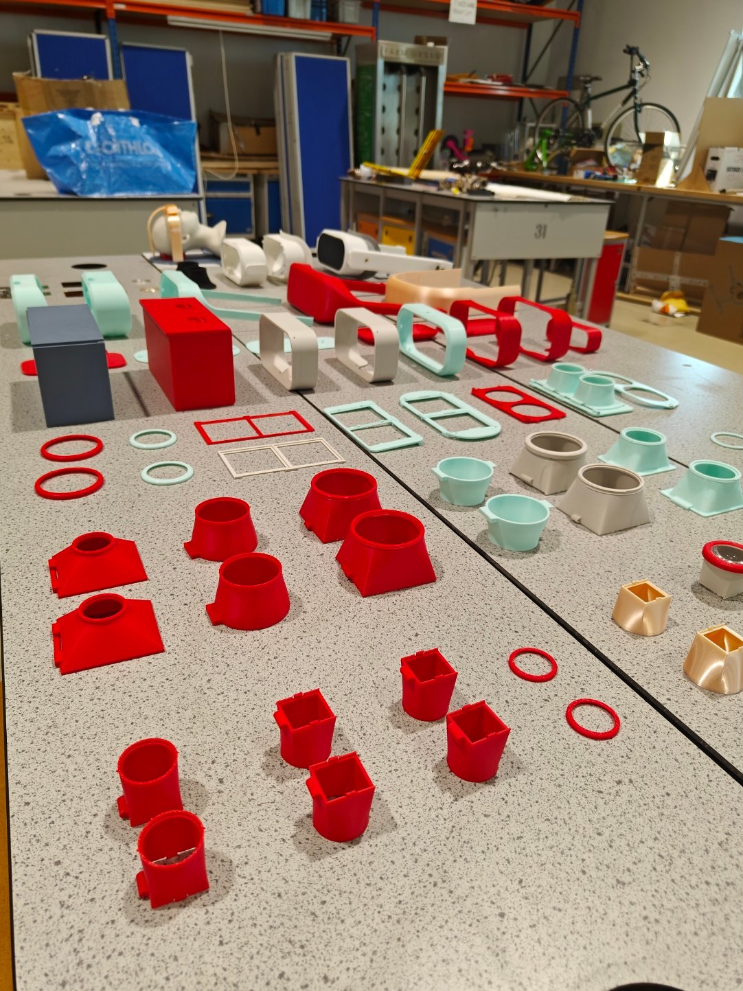 A workshop bench covered in dozens of 3D-printed IRIS parts in red, white and mint: housings, lens cones and mounts